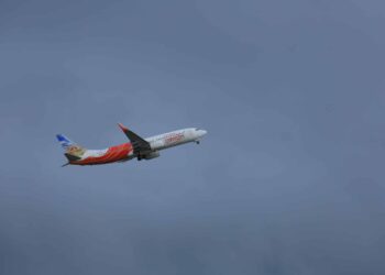 An Air India Express plane flies with a cloudy sky in the background