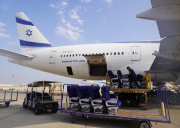 Passenger seats sit on a trolley, being taken away from a plane with the Israeli flag on its tail