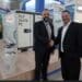 Miguel Rodriguez and Akos Balkanyi shake hands in front of an Envirotainer container